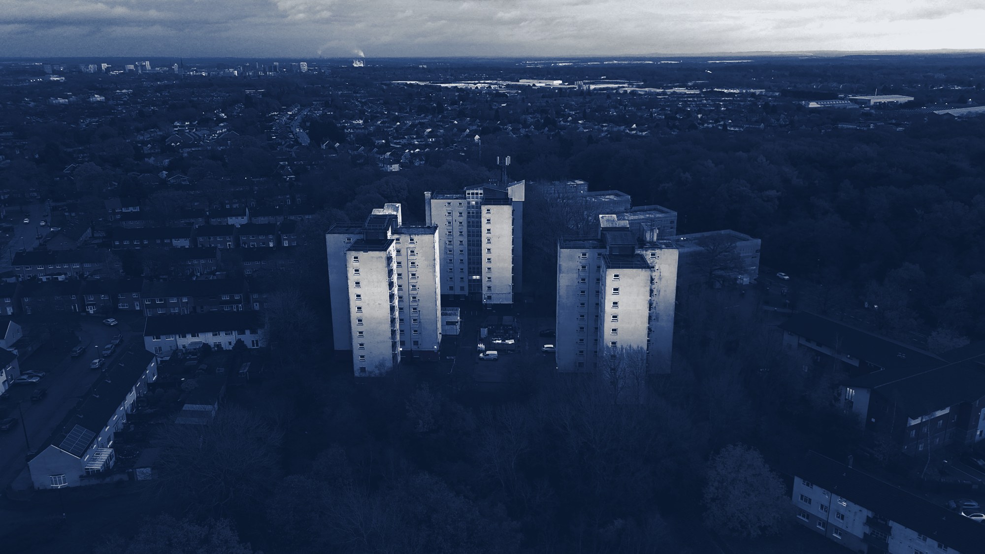 Apartment blocks among trees at dusk, tinted navy
