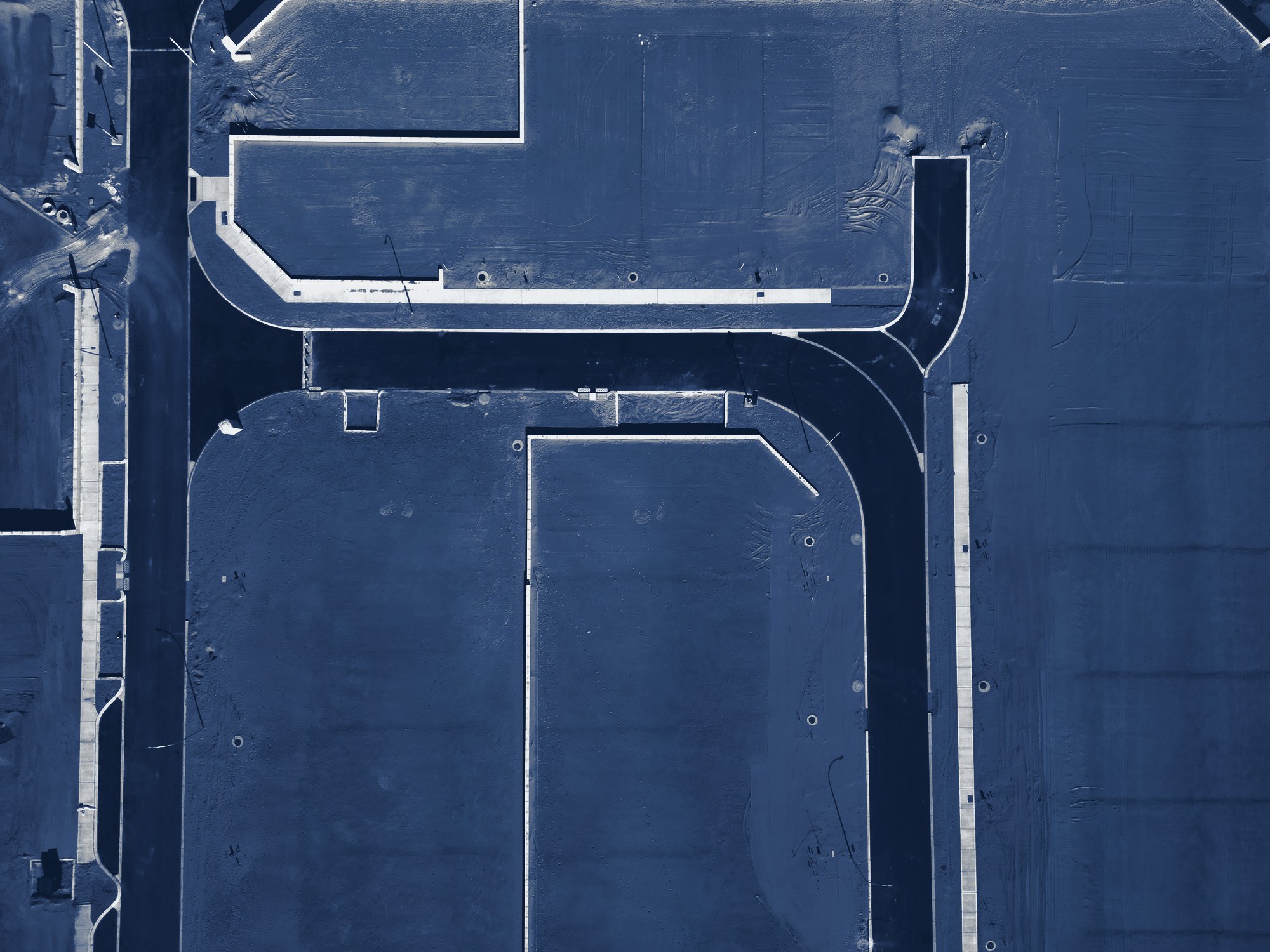 Top-down aerial of graded land with newly paved subdivision streets and curbs, lots not yet built, tinted navy