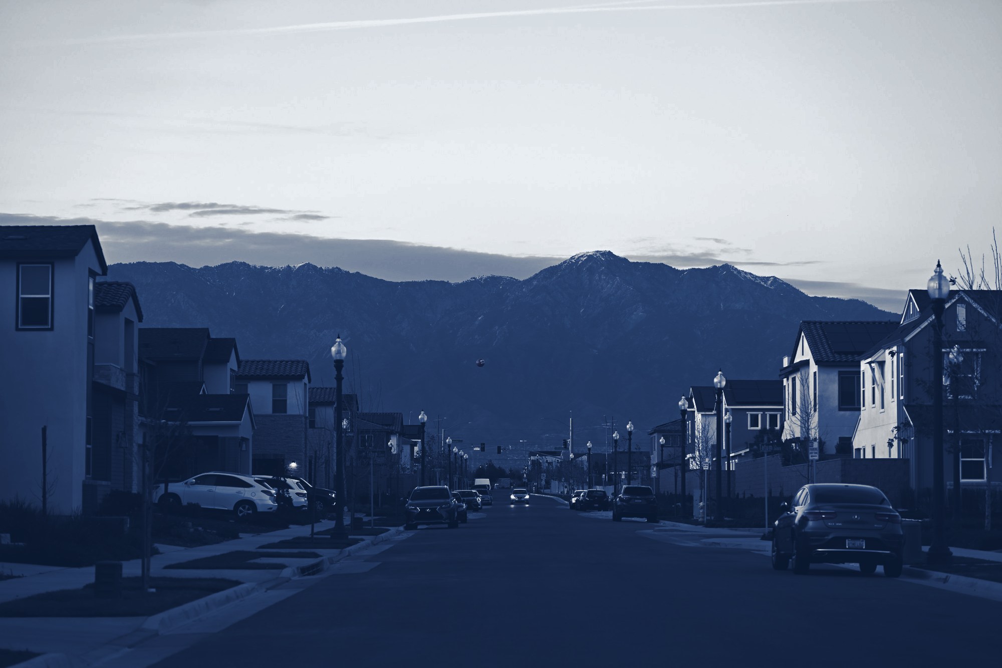 New suburban street lined with two-story single-family homes at dusk, mountains behind, tinted navy