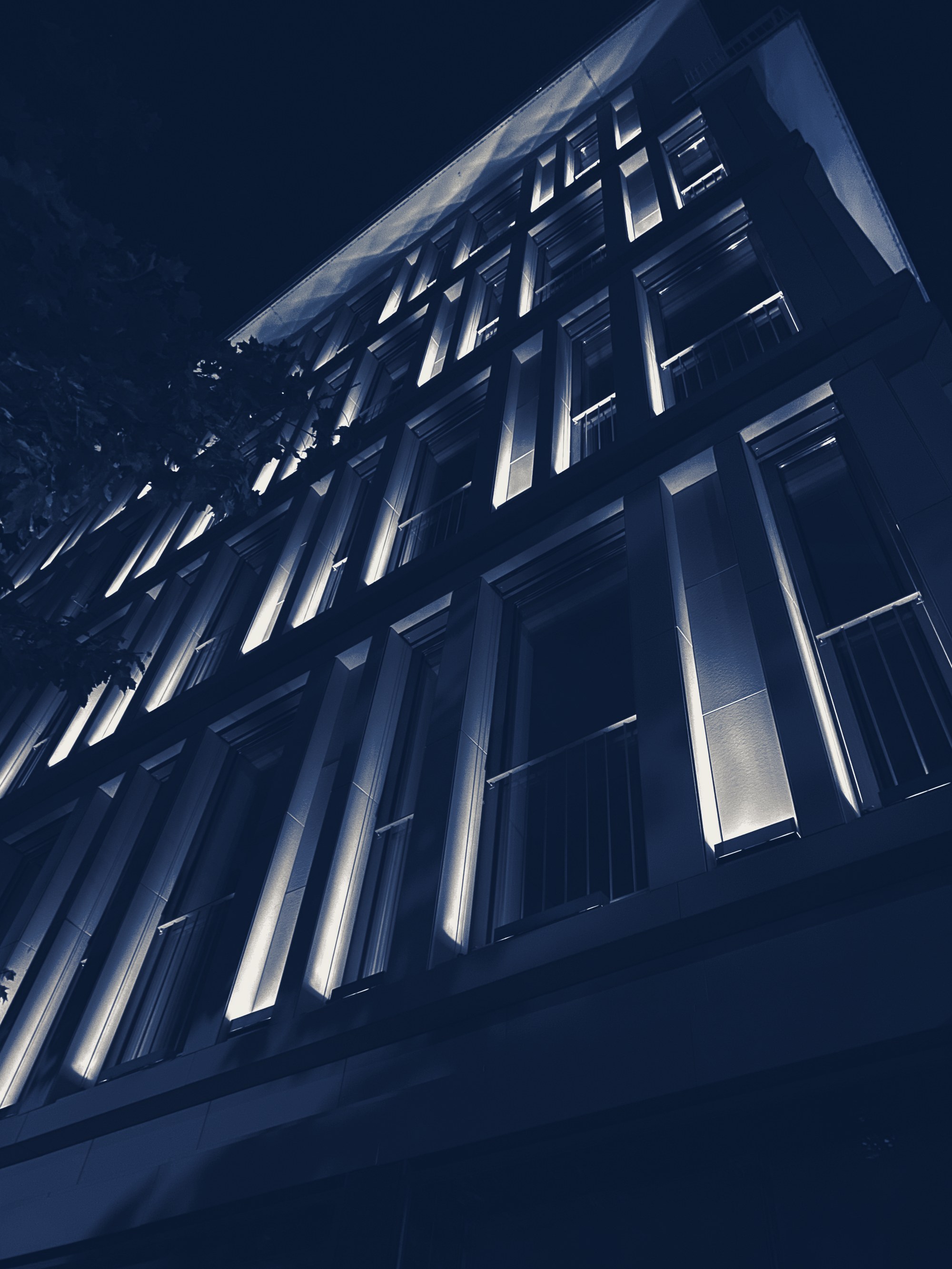 Residential building facade lit at night, tinted navy