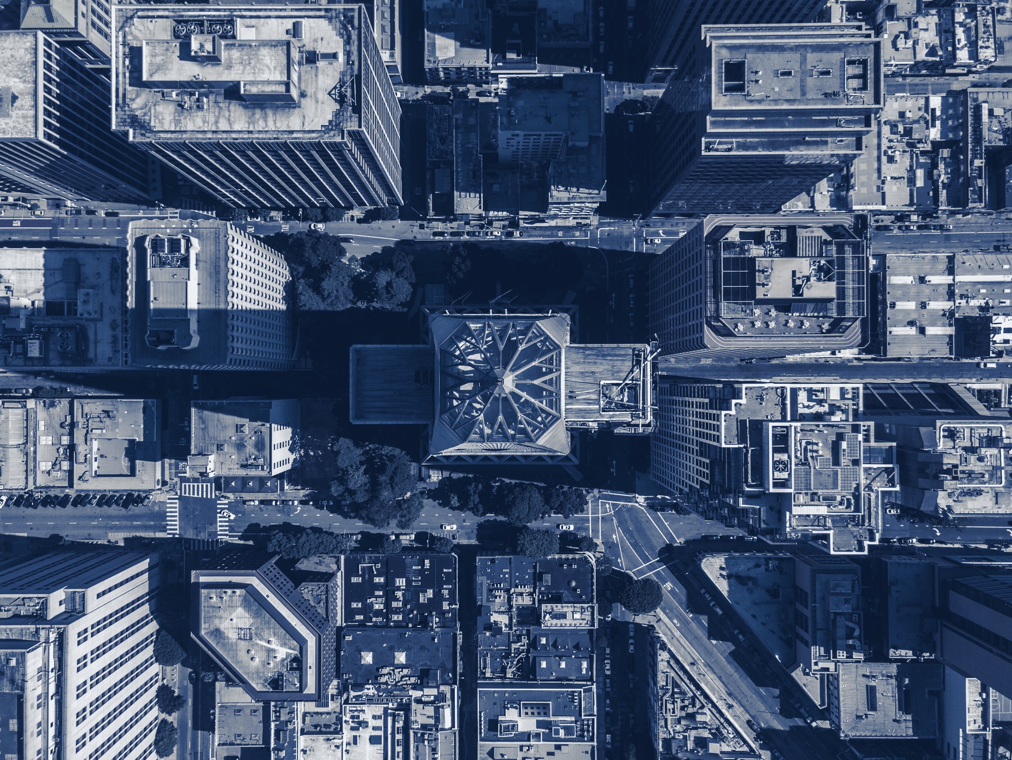 Straight-down aerial of a downtown district: towers, mid-rise and low-rise buildings, a glass-roofed landmark, streets and trees, tinted navy