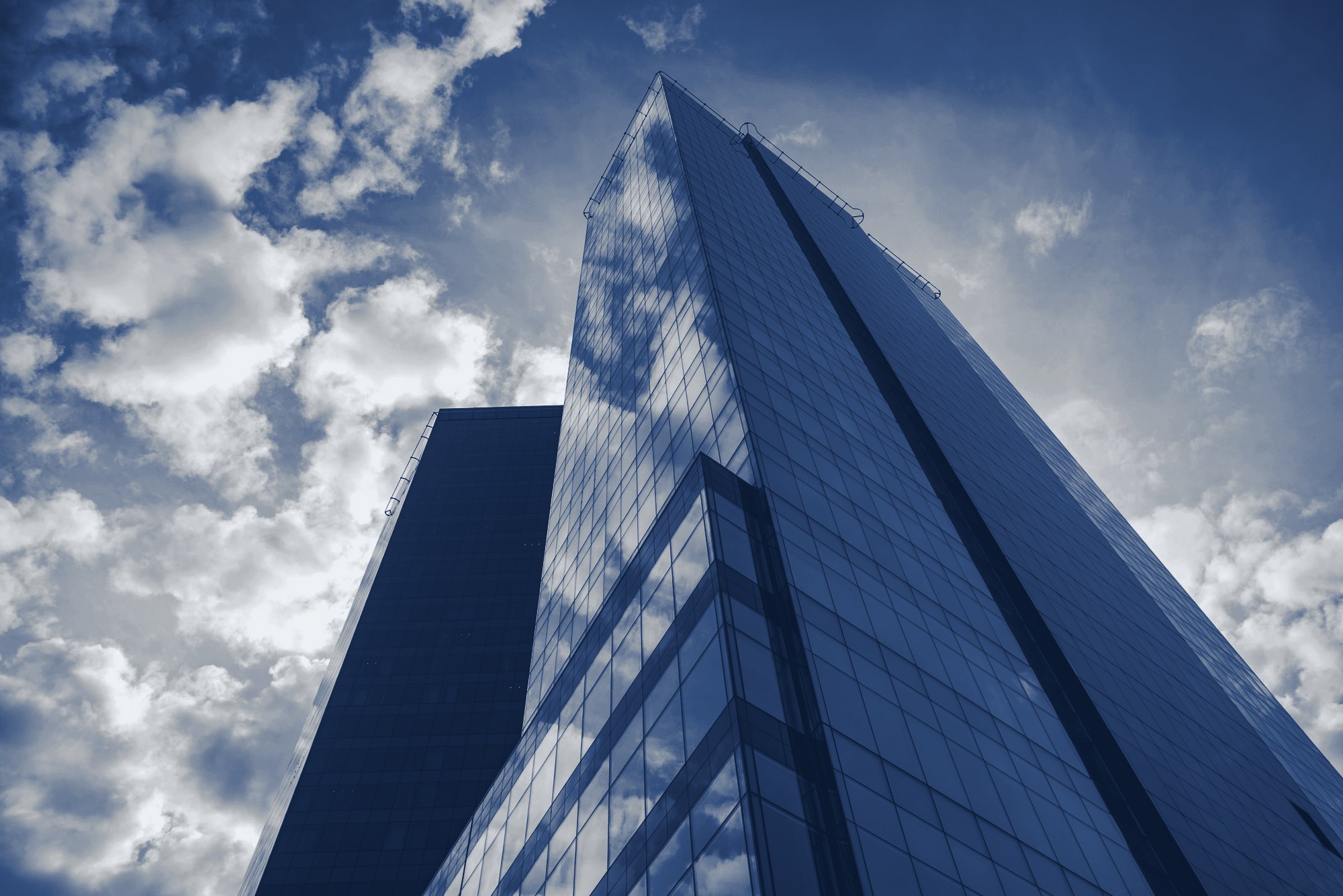 Low-angle view of a glass Class A office tower against a cloudy blue sky, tinted navy