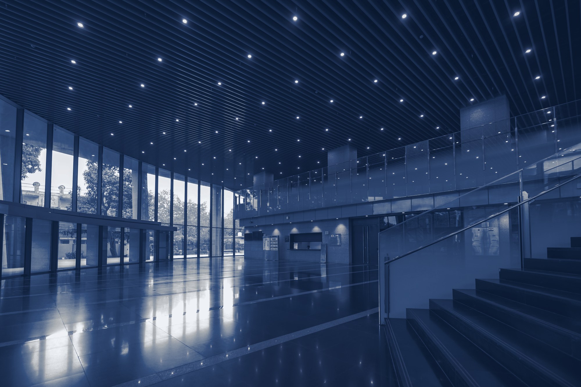 Empty modern lobby with polished floor, window wall, staircase and a front-desk window at the back, tinted navy