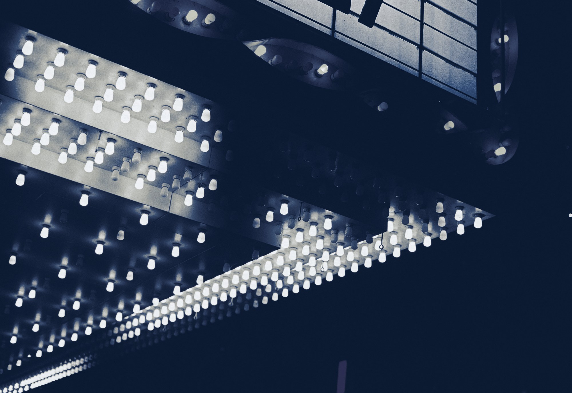 Close-up of a theater marquee underside lined with glowing bulbs at night, tinted navy